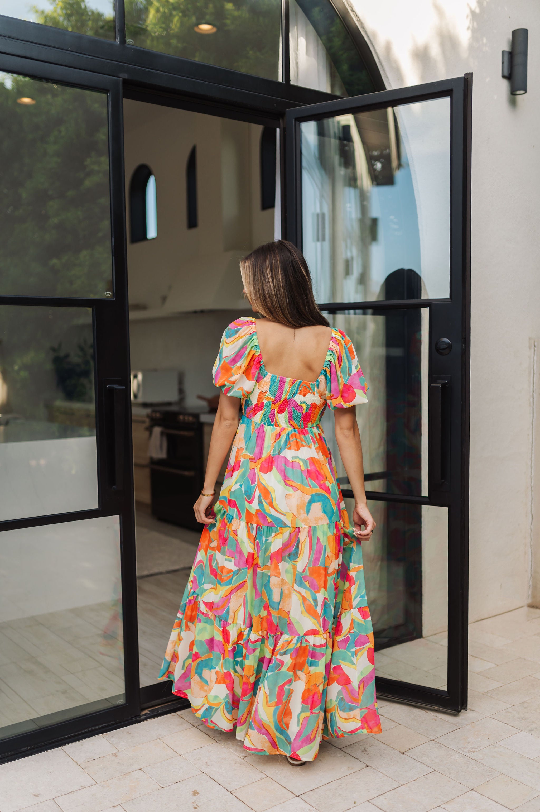 Rear view of  Isle Glow Maxi Dress in allover bright floral print with short puff  sleeves, smocked back, and ruffle hem. 